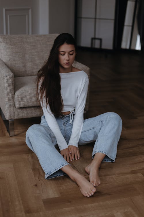 Long Haired Brunette Woman in Light Blue Jeans and White Top Sitting on the Floor 
