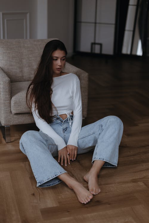 Long Haired Brunette Woman in White Top and Blue Flared Jeans Sitting on the Floor