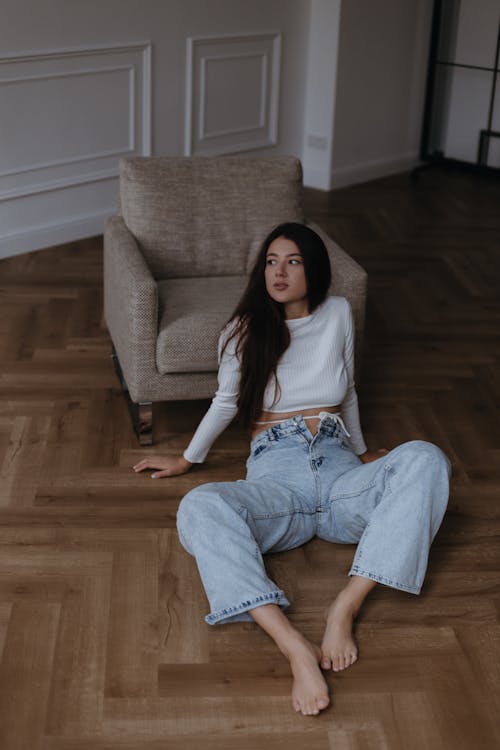 Young Woman in White Long Sleeved Top and Blue Flared Jeans Sitting on a Floor