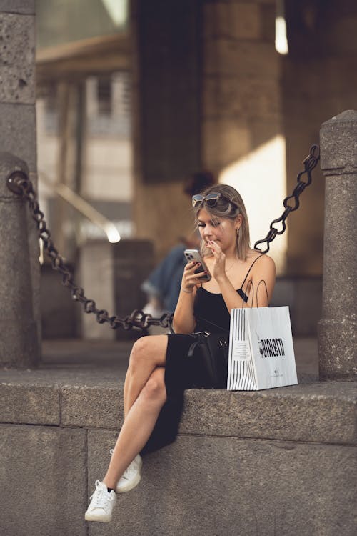Woman in Black Dress Sitting with Smartphone and Bag