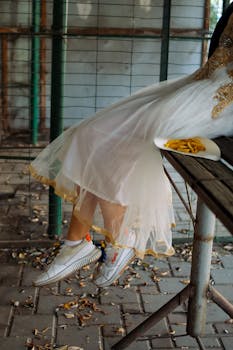 A stylish woman in a white dress and sneakers sits on a bench with french fries.