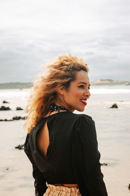 A woman with curly hair smiles while enjoying a breezy day at Pipa Beach, Brazil.