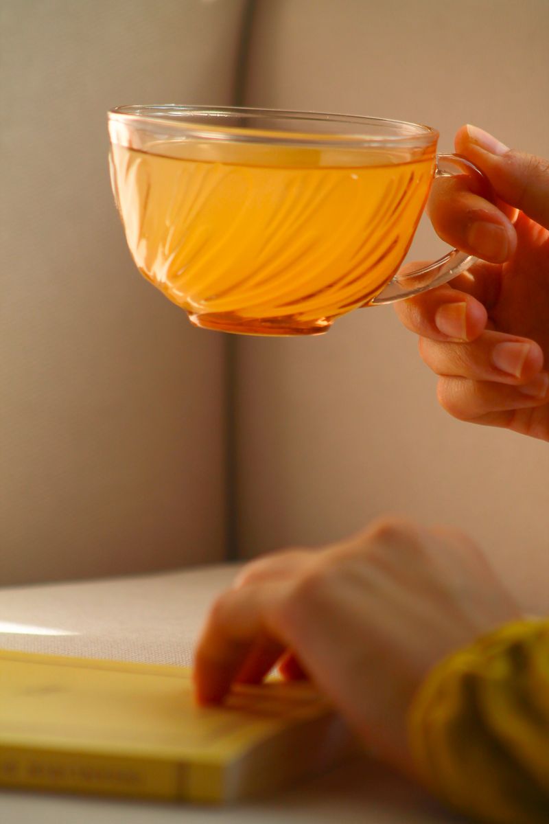 Hands cradling a warm cup of tea beside a book