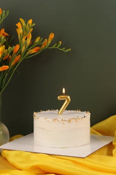 Elegant lemon cake with a golden number seven candle and vibrant flowers.