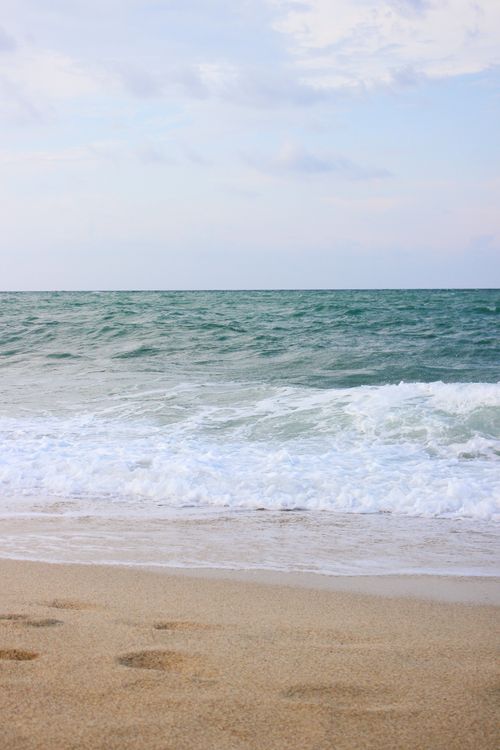 Free Tranquil beach scene with gentle waves and soft sand under a pastel sky. Stock Photo