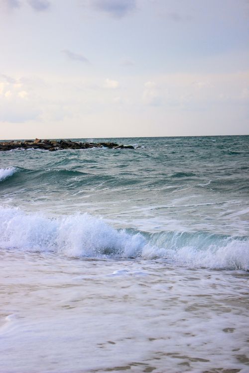 Free Peaceful coastal scene featuring waves crashing on the sandy shore under a bright sky. Stock Photo