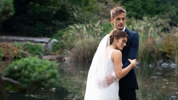 Young Newlyweds Hugging by a Pond in the Park