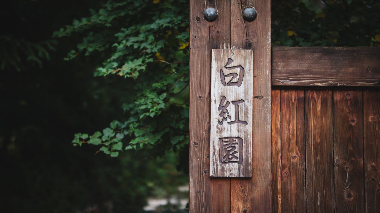 close up of a wooden sign with japanese characters in a garden in wroc