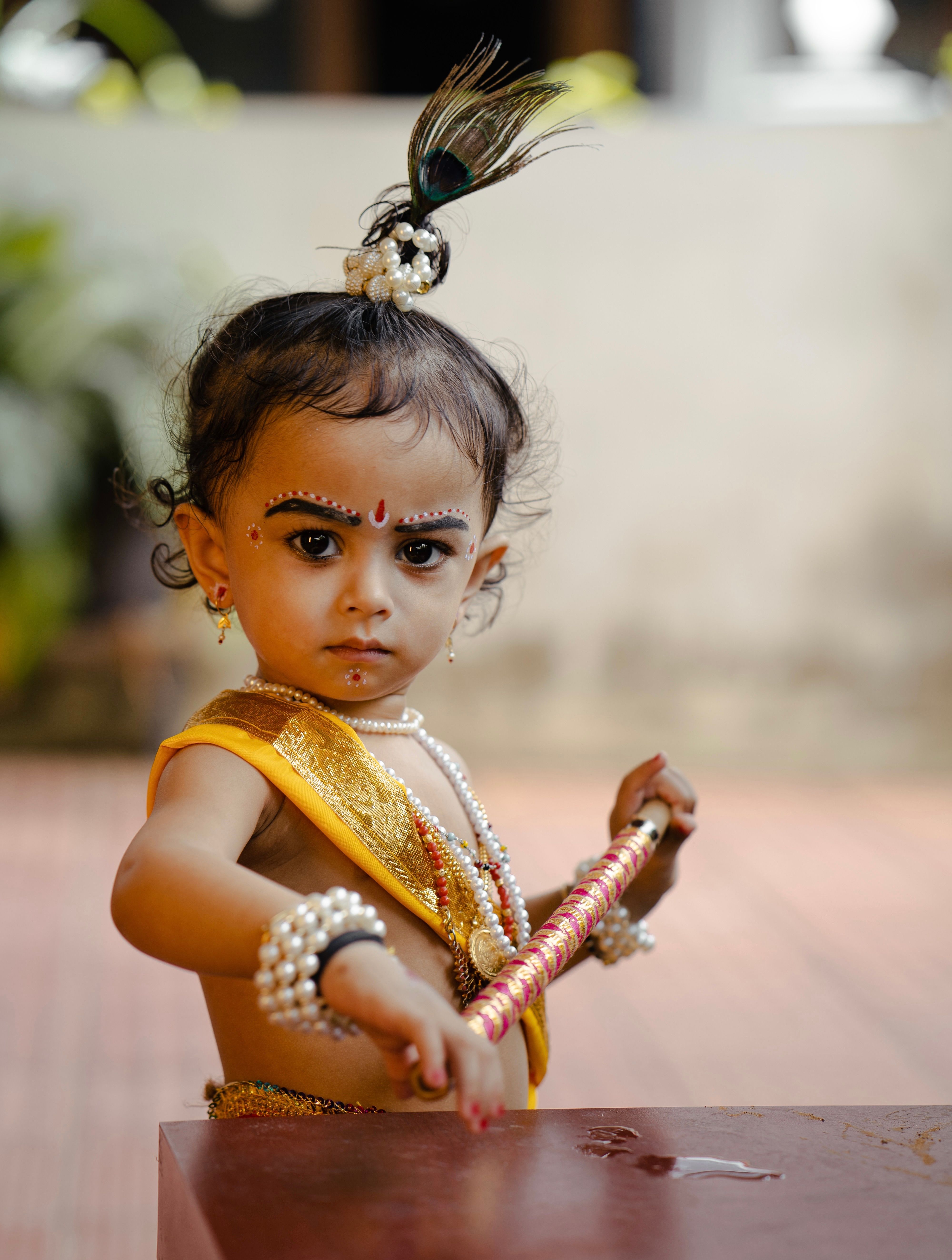 A young child in traditional Indian attire, adorned with jewelry and holding a stick, posing outdoors.