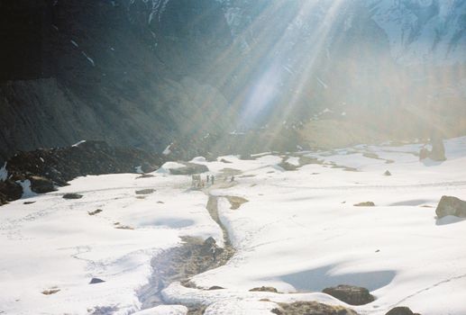Group of hikers trekking a snow-covered trail with sunbeams streaming in a mountainous landscape.