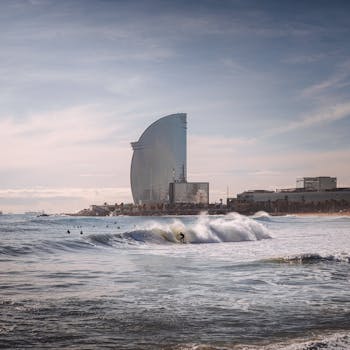 Surfer navigating waves with the backdrop of the iconic W Barcelona Hotel on a sunny day. by Valdemaras D.