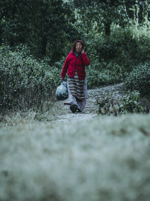 Elderly Woman Carrying Bags Walking Along a Forest Path