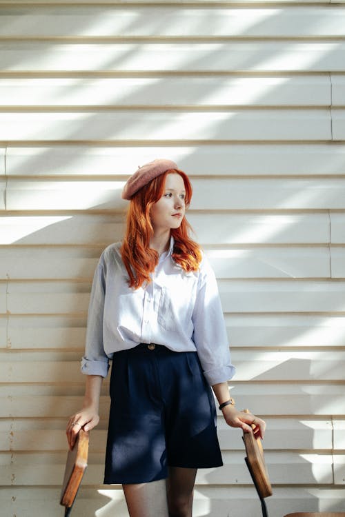 Free Portrait of a Pretty Redhead Wearing a Beret Standing against a White Wall Stock Photo