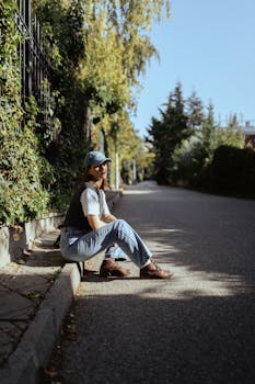 Casual young woman sitting on a sunlit city street, showcasing a stylish outfit perfect for a casual day out.