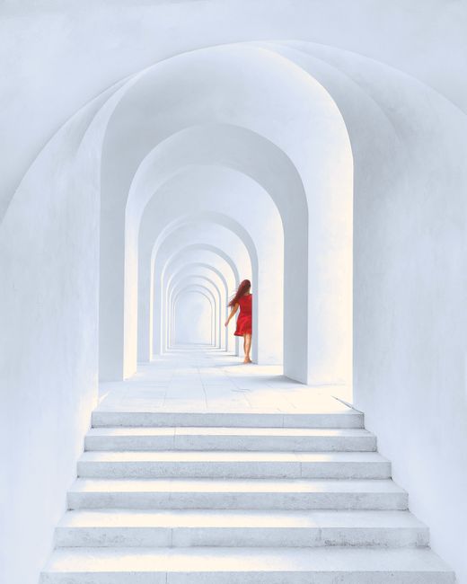 A woman in a red dress walks through a series of white arches, creating a stunning contrast and leading lines.