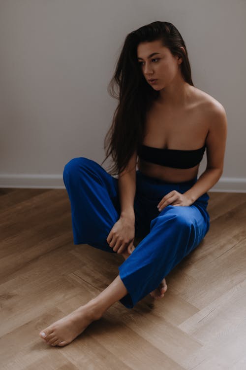 Young Brunette Woman in Blue Pants and Black Bandeau Top Sitting on the Floor