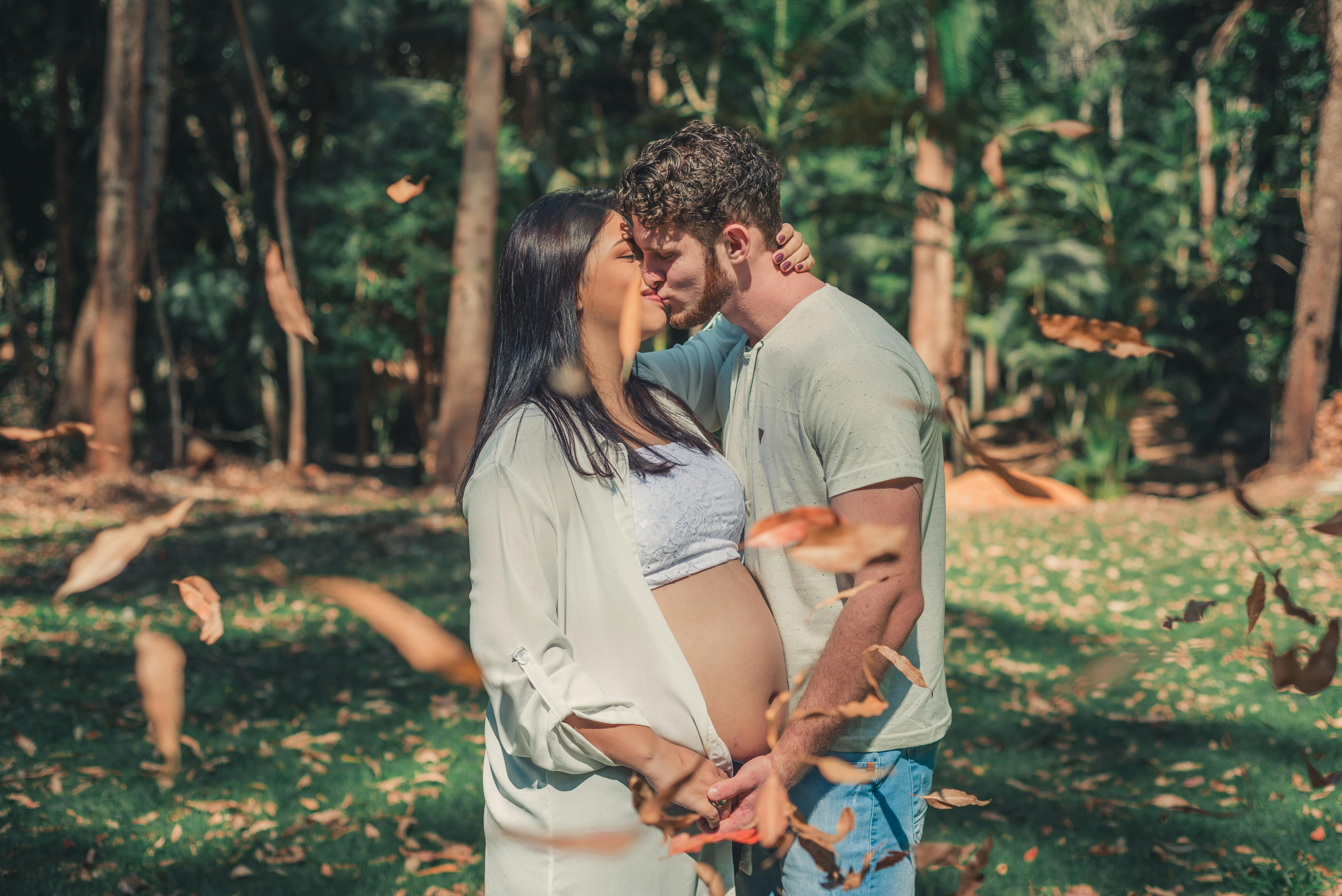 pregnant woman and man kissing front of the tree