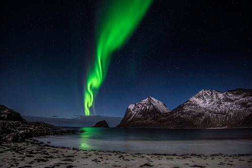 Free Stunning view of green aurora borealis illuminating the night sky over snowy mountains and ocean. Stock Photo