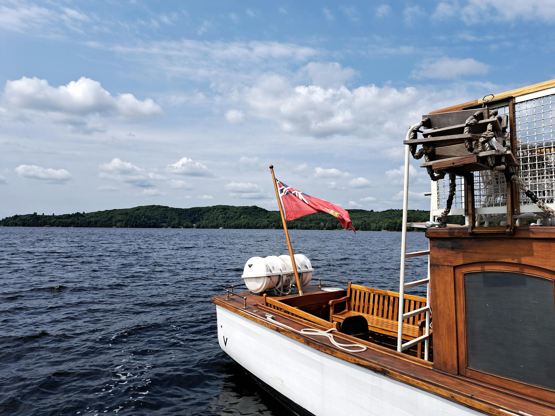 A classic wooden motorboat with a red ensign flag on a lake in Dwight, Ontario under a bright sky.