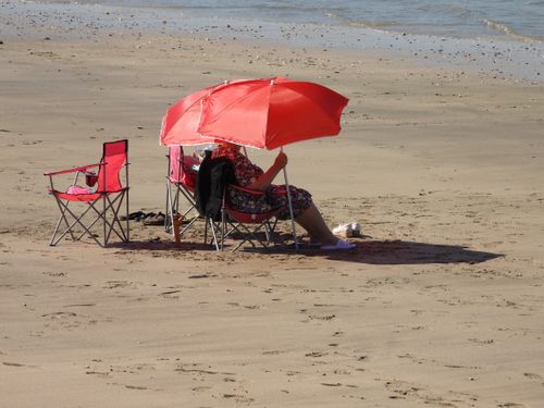 Free A woman relaxes under a red umbrella on Berck Beach, France, enjoying a sunny day. Stock Photo