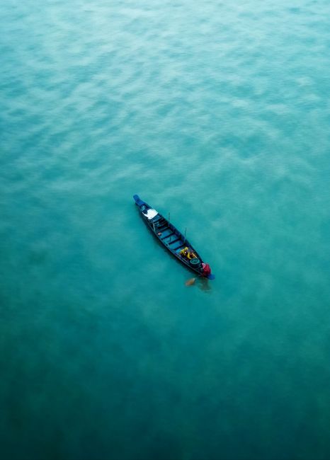 A lone fishing boat floats on the tranquil waters of Chattogram, Bangladesh, captured from above.