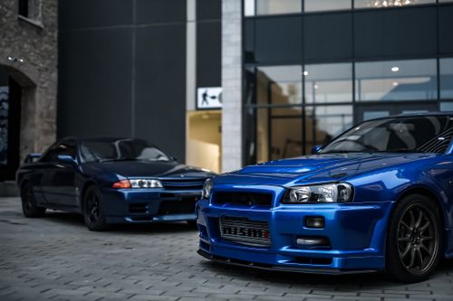 Free Two blue sports cars parked on the pavement outside a modern glass building. Stock Photo