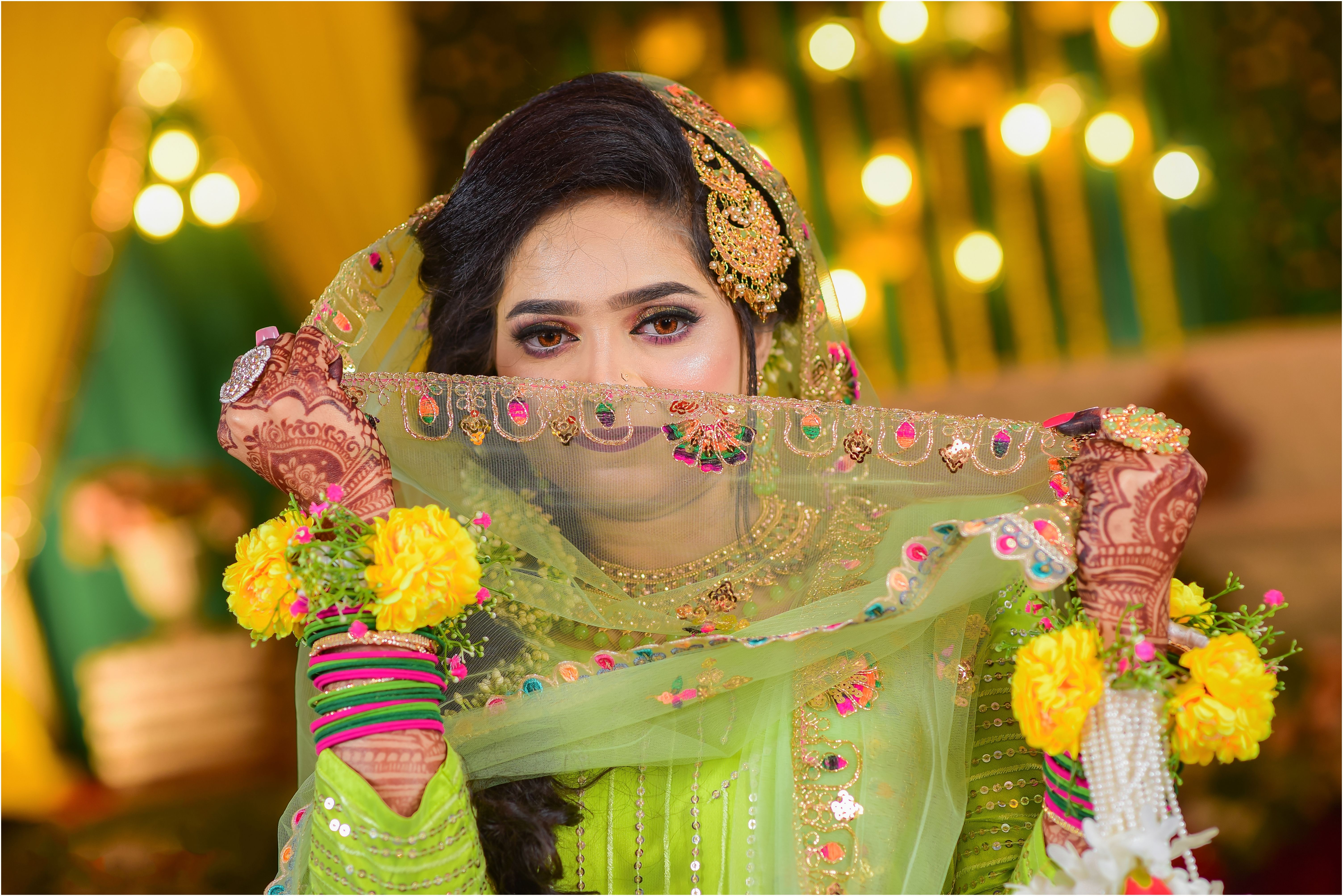 A bride poses with henna tattoos in a vibrant wedding ensemble.