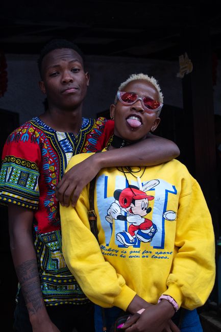 Stylish young African American duo posing playfully, embracing vibrant fashion in an urban setting.