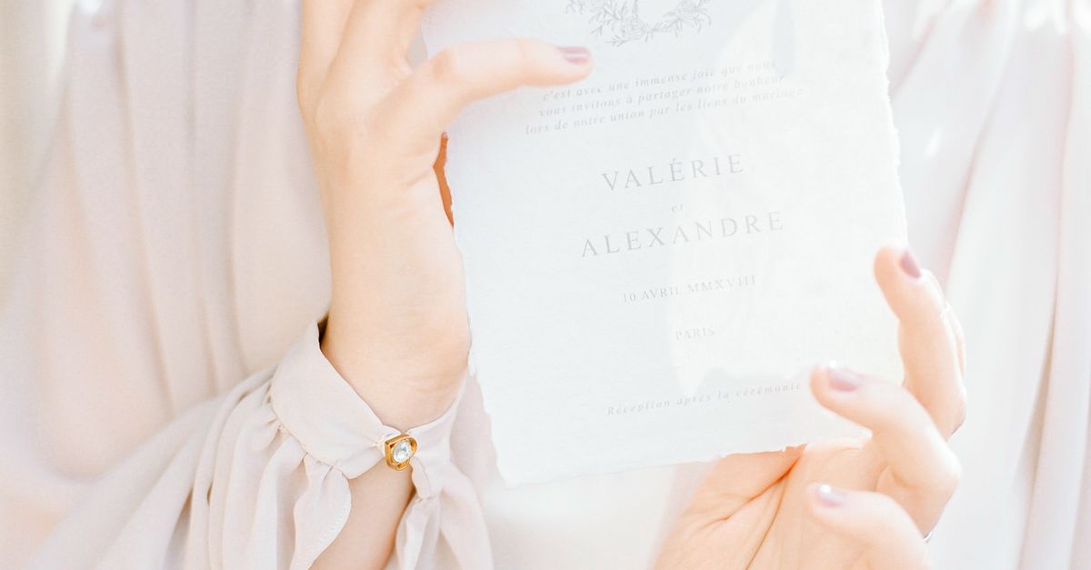 Close-up of a woman elegantly holding a wedding invitation in soft lighting.