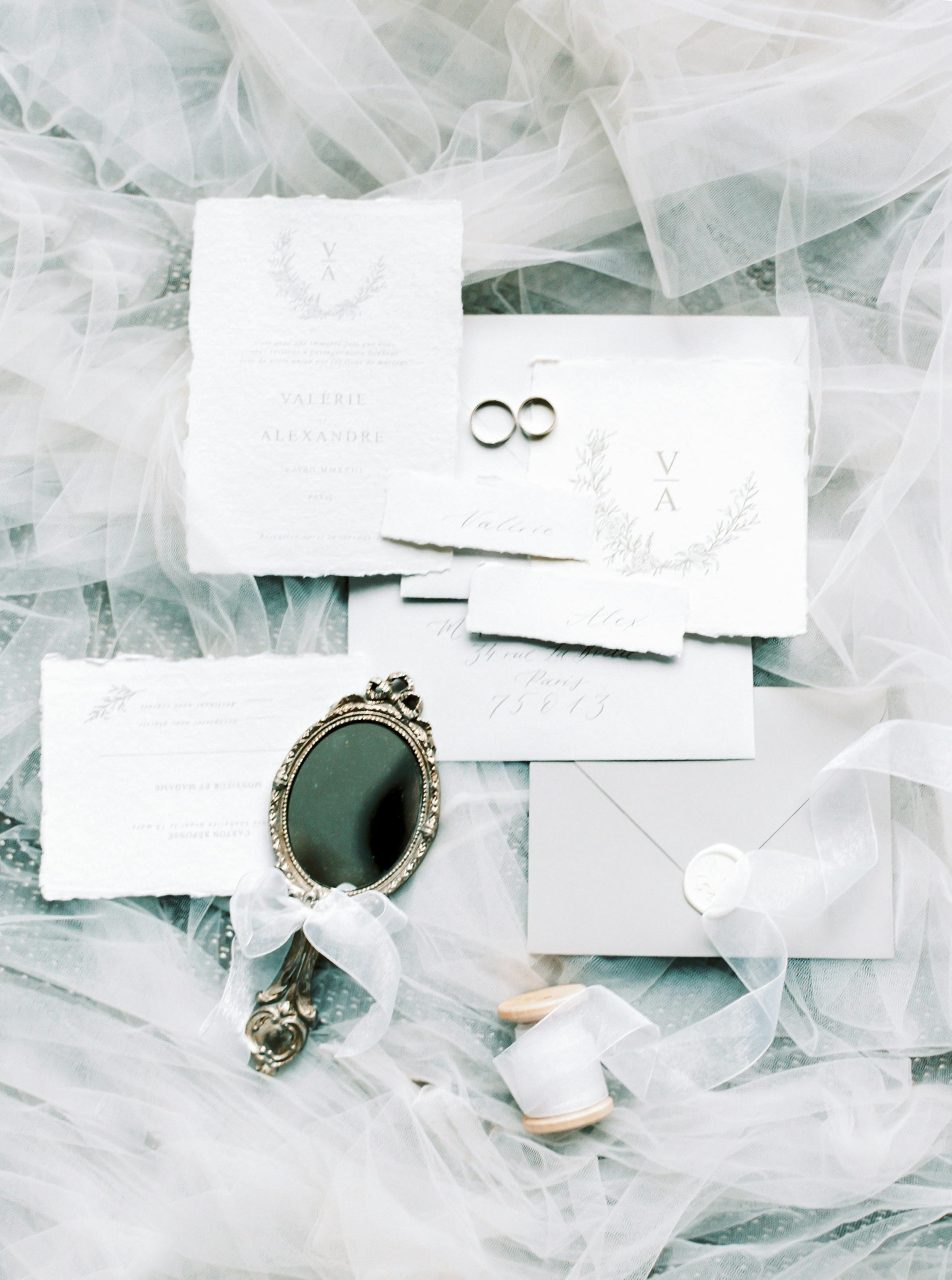 Charming flat lay featuring wedding invitations, rings, and a vintage mirror on delicate fabric.