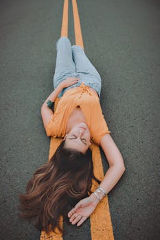 一位身着休闲装的女士躺在黄纹鲜艳的道路上，尽显时尚与风格