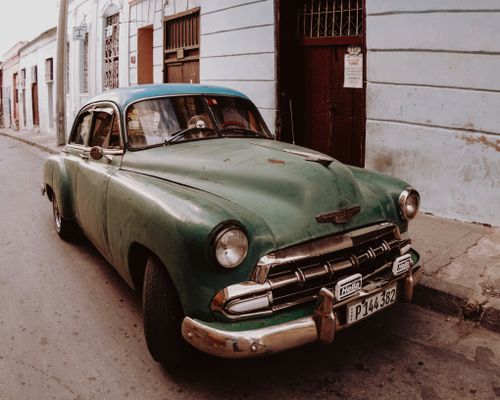 Free A retro green vintage car parked on a historic urban street, evoking a classic ambiance. Stock Photo