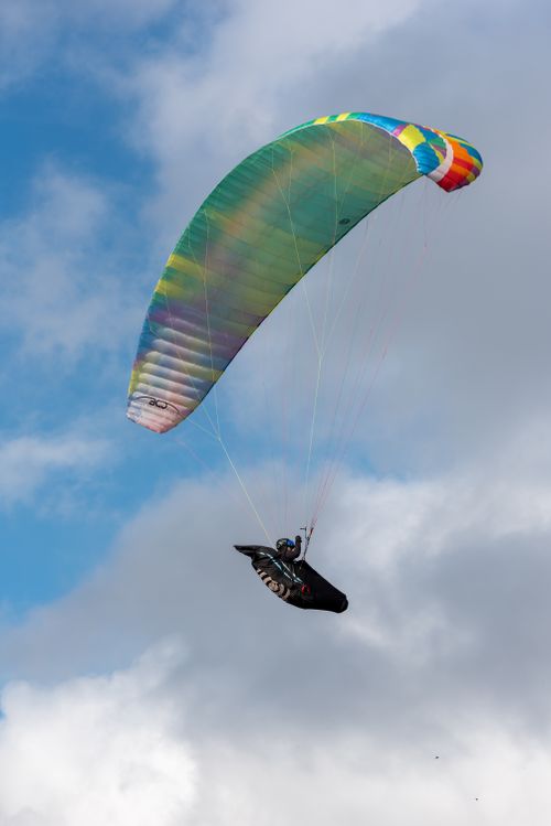 Free Paraglider soaring beautifully through blue skies with a vibrant parachute, perfect for adventure seekers. Stock Photo