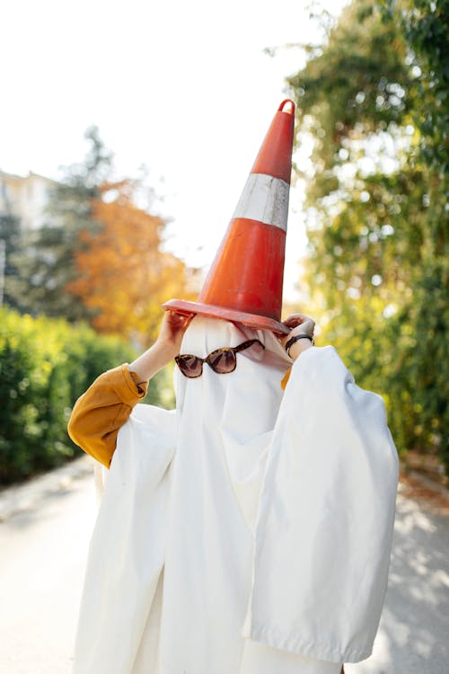 Person Covered in a White Sheet Wearing Sunglasses and a Traffic Cone