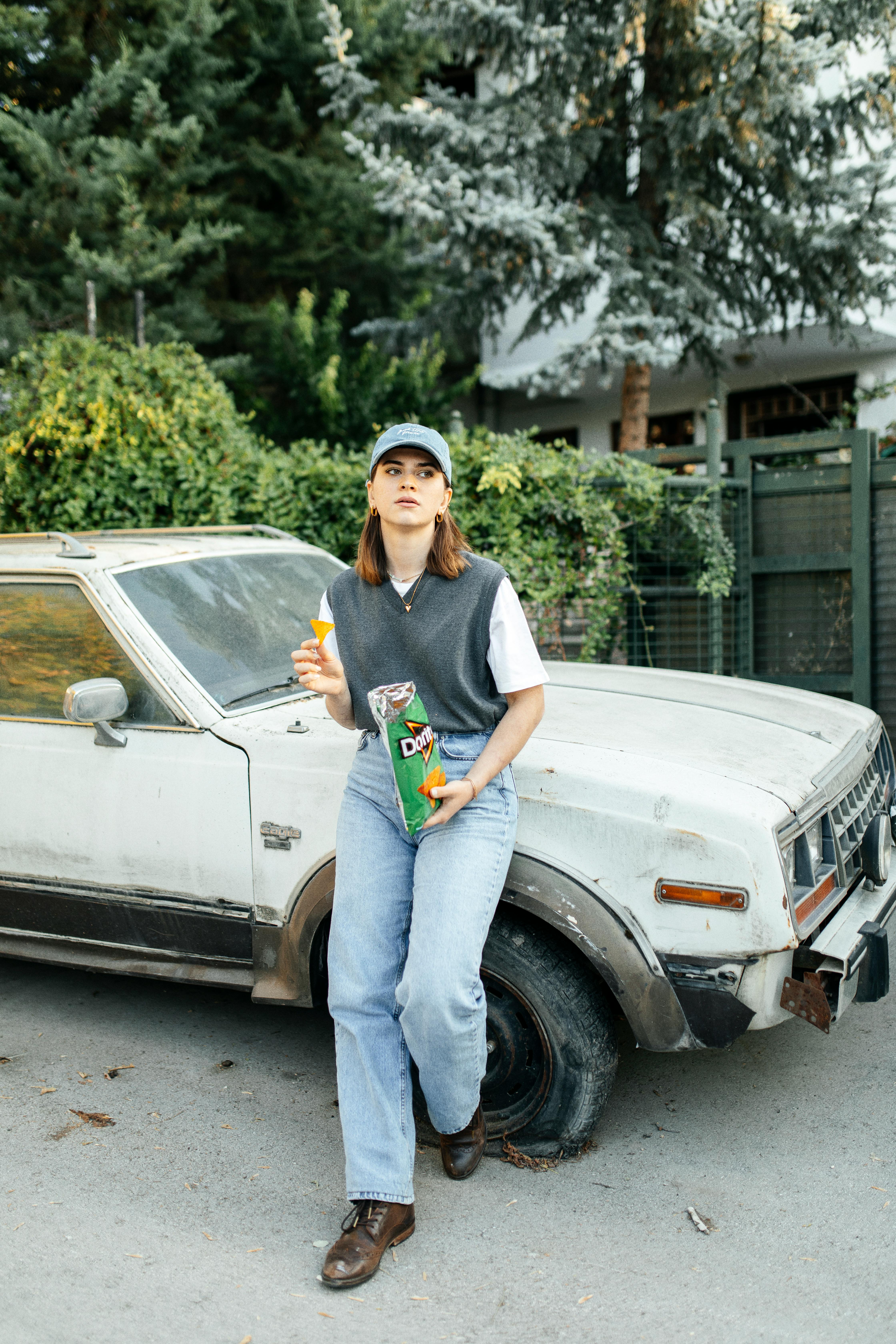 Woman in Cap Standing by Car and Eating · Free Stock Photo