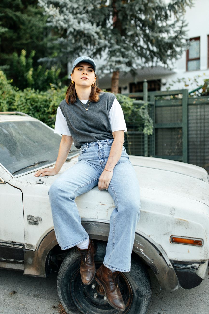 Stylish woman in casual attire sitting on a vintage car outdoors. Perfect for urban lifestyle themes.