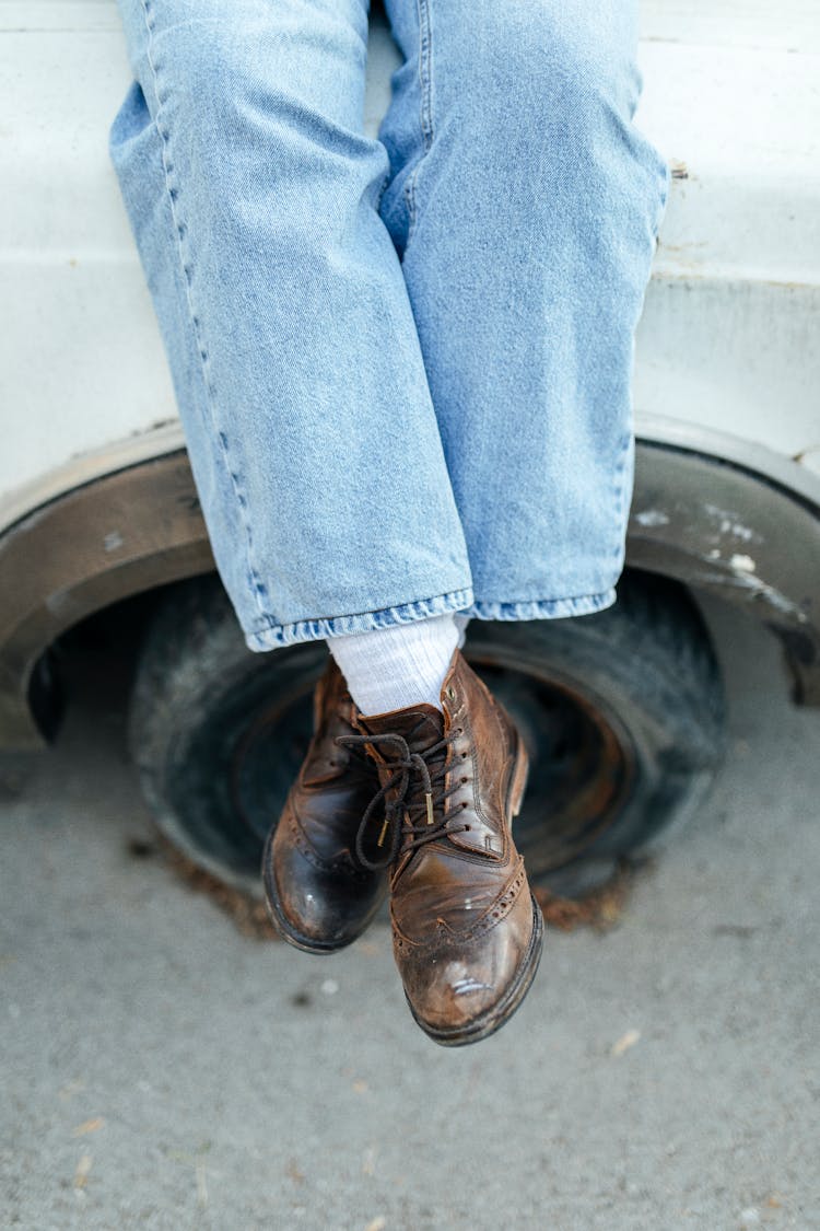 Legs Of A Person Wearing Brown Leather Boots Sitting On Top Of A Parked Car