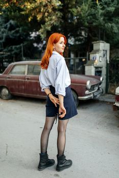 Stylish woman with red hair in urban setting wearing shorts and boots.