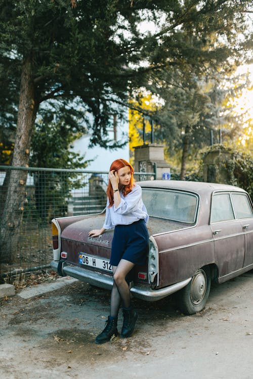 Woman in a Shirt and Shorts Fixing her Hair while Leaning on a Car Hood