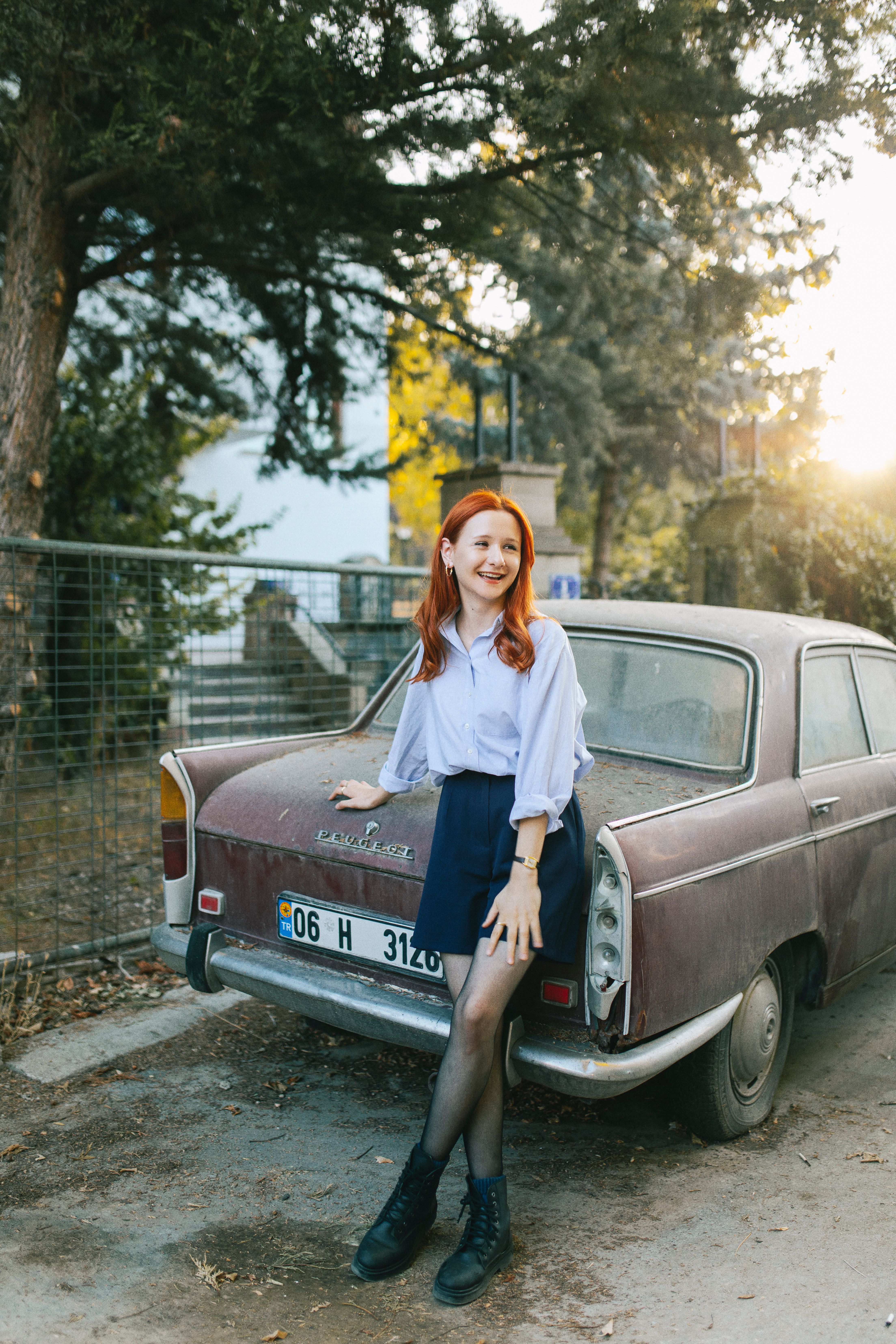 Stylish young woman posing by a vintage car in a sunlit urban setting.