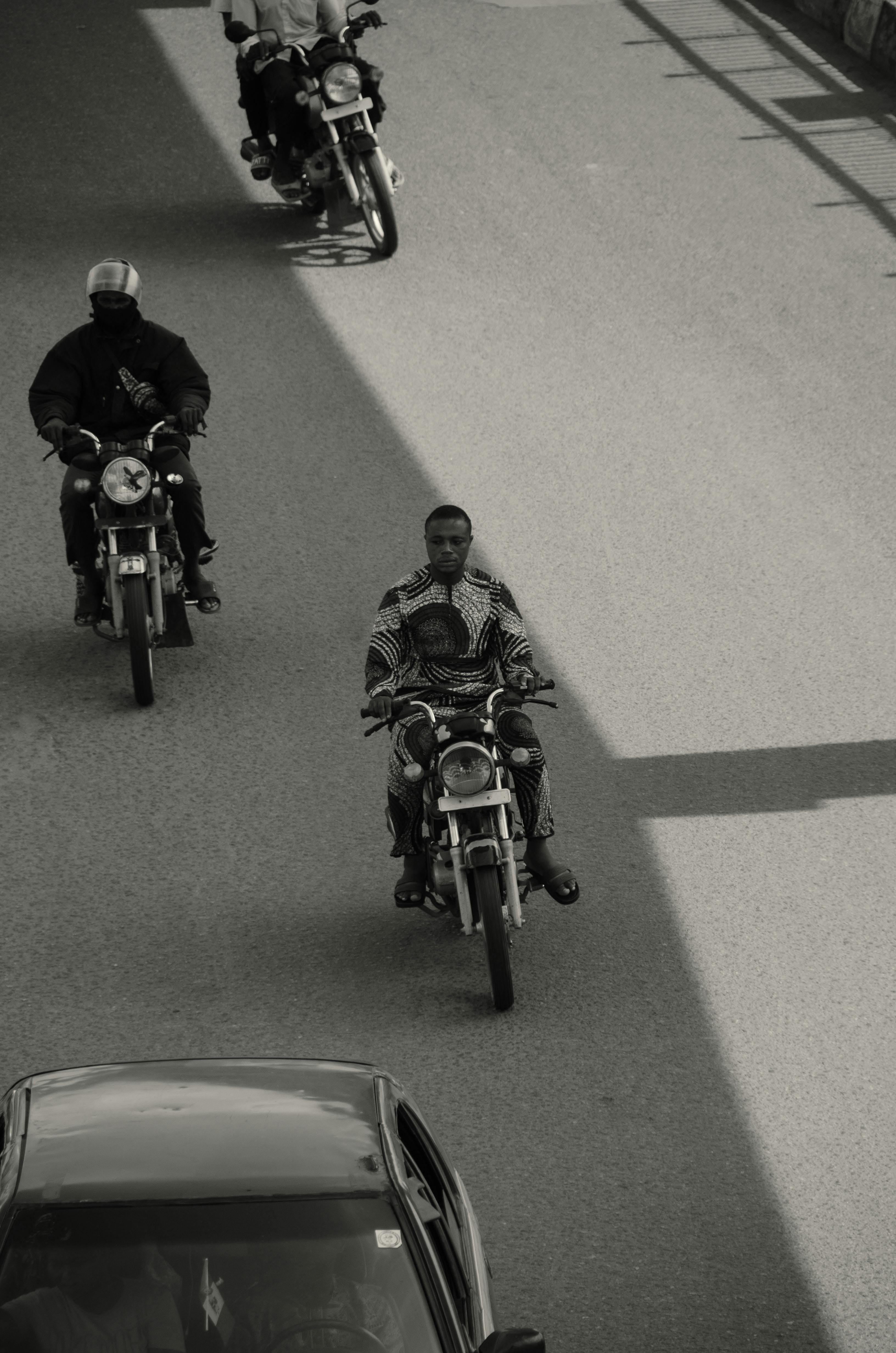 Black and white image of motorcyclists riding on a city street, photographed from above.