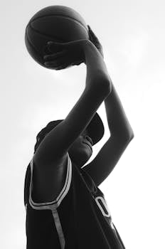 Black and white photo of a basketball player poised to shoot the ball outdoors.