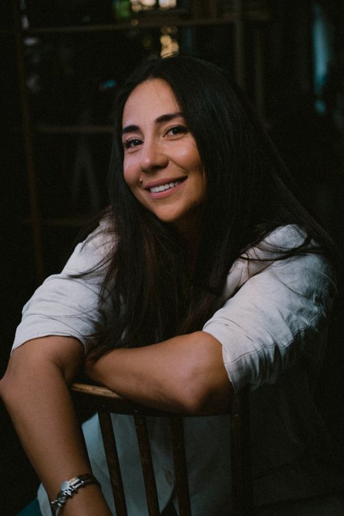 Free Portrait of a brunette woman with long hair sitting and smiling indoors. Stock Photo