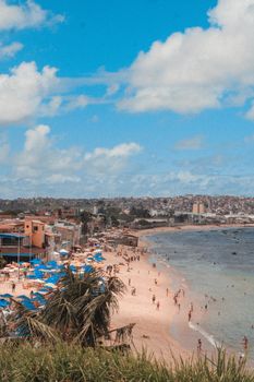 A beautiful coastal view showcasing a bustling beach and urban backdrop under a bright blue sky.