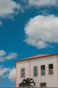 A charming white building with a red tile roof under a vibrant blue sky with fluffy clouds.