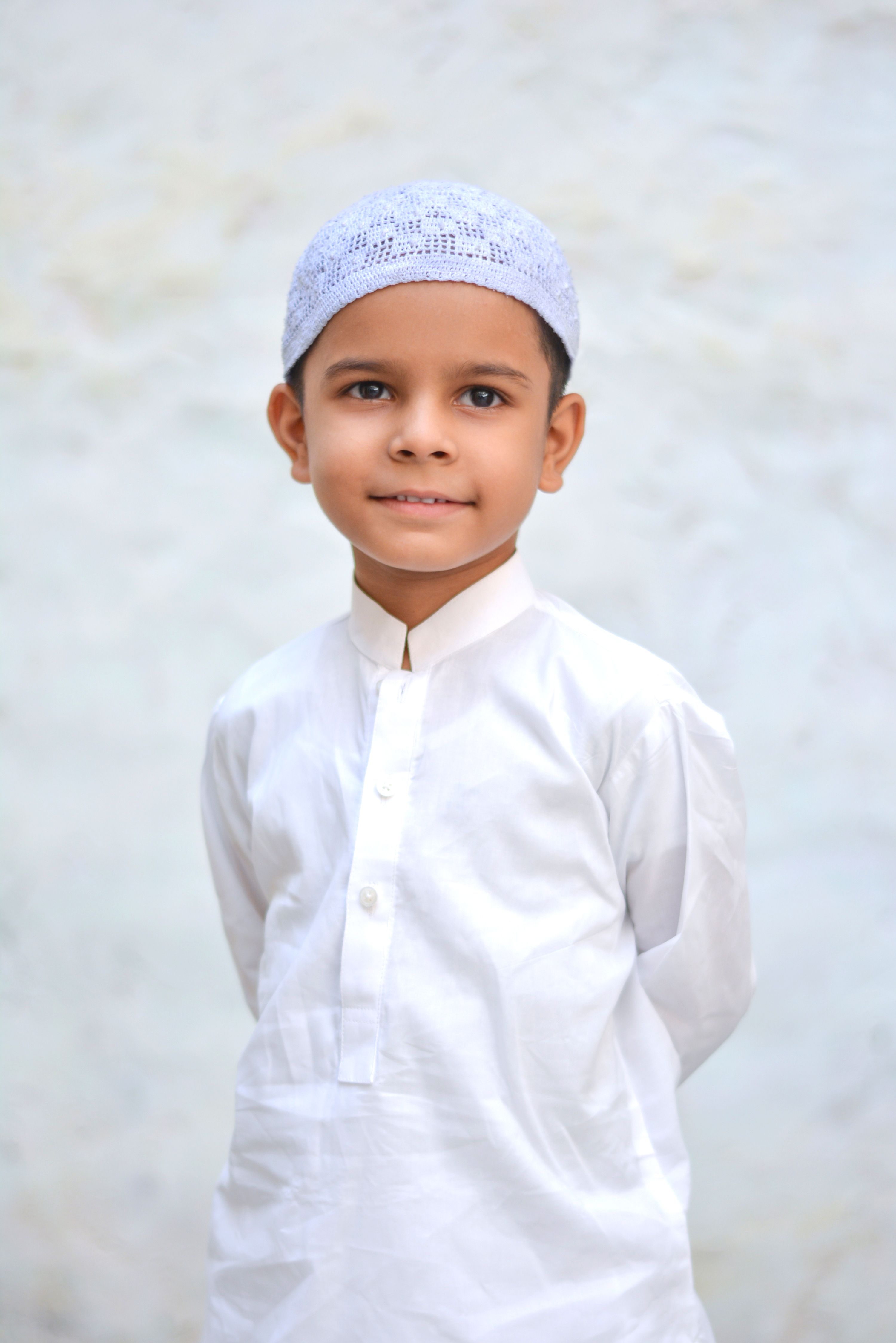 Charming portrait of a young boy in white traditional clothing against a plain background.