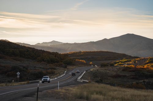 Free Cars travel on a winding highway through a mountainous landscape during an autumn sunset. Stock Photo