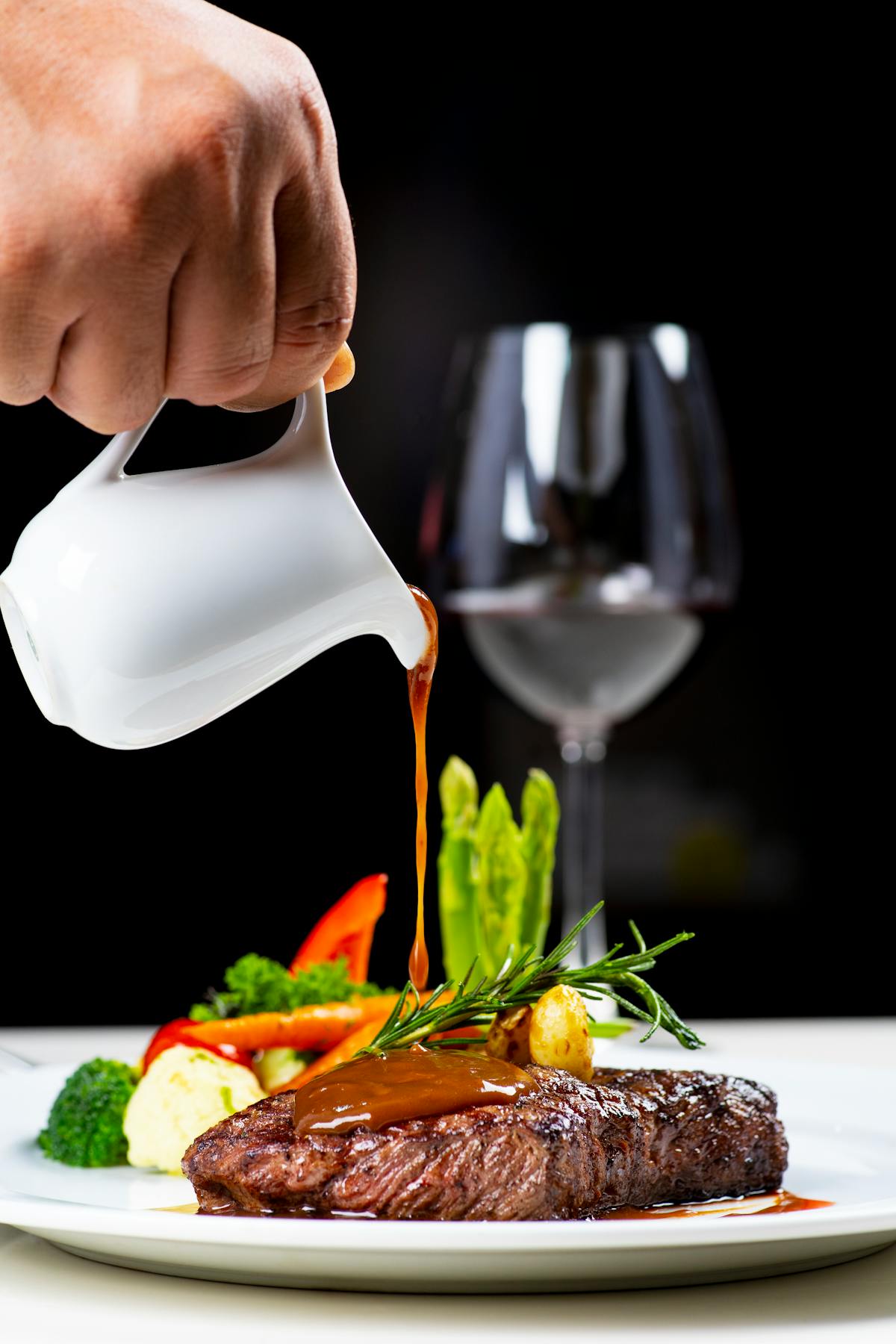 Salsa versata su una succulenta bistecca con verdure e vino rosso