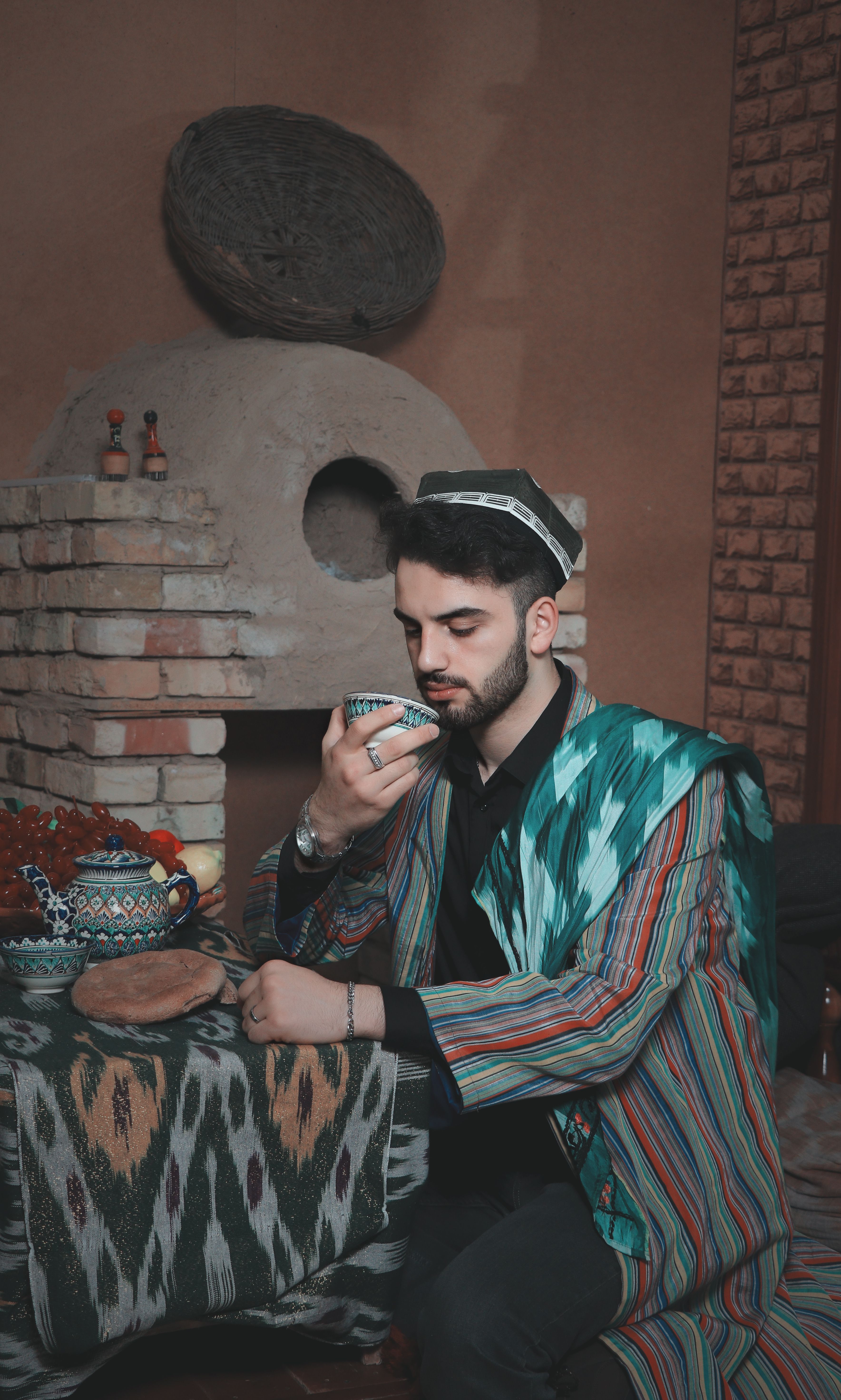 A man in traditional attire enjoys a warm drink in an ornately decorated room.