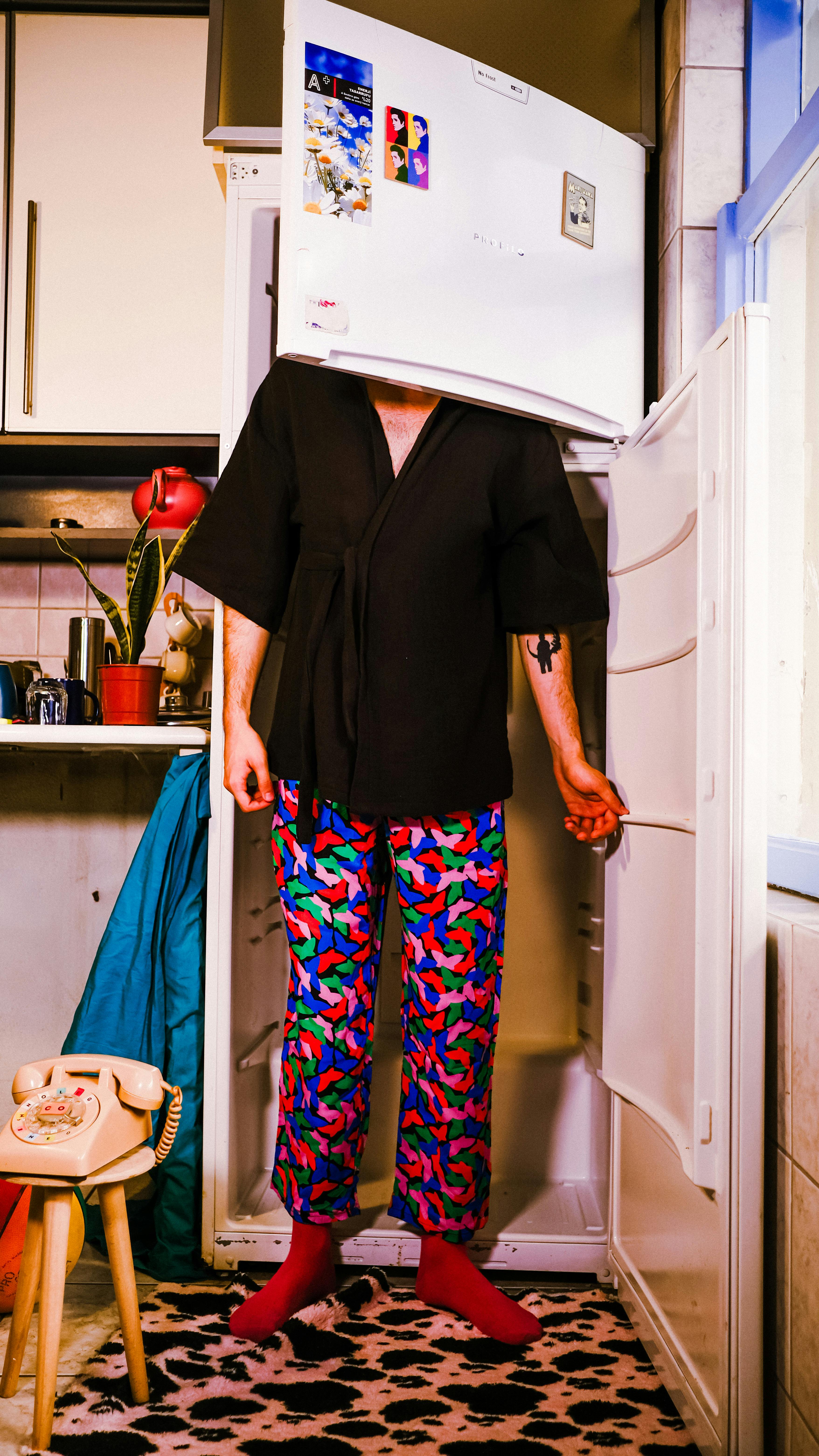 Artistic fashion pose with a man humorously posing inside a refrigerator in colorful pants.